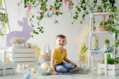 Mutlu çocuk Paskalya stüdyosunun ahşap zemininde oturur. Çiçekler, ahşap tavşanlar, yumurtalar...