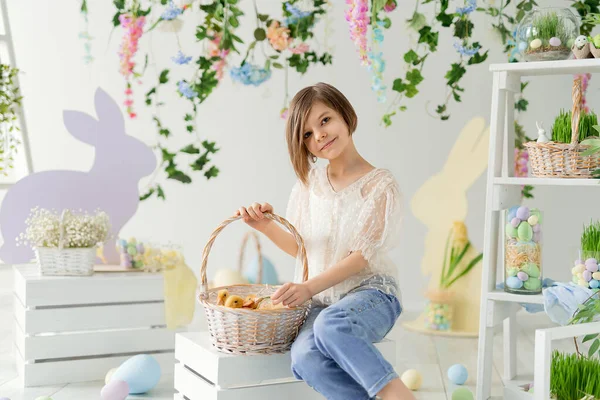 Cute girl holds the basket with fluffy ducklings while sits on the wooden box. Easter decoration. — Stock Photo, Image