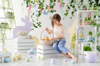 Küçük kız, tahta kutunun üzerinde otururken ördek yavrularıyla sepetin içinde iletişim kuruyor. Paskalya dekorasyonu