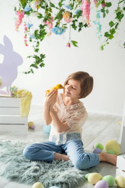Küçük kız yerde otururken ördek yavrusuyla iletişim kuruyor. Paskalya dekorasyonu. 