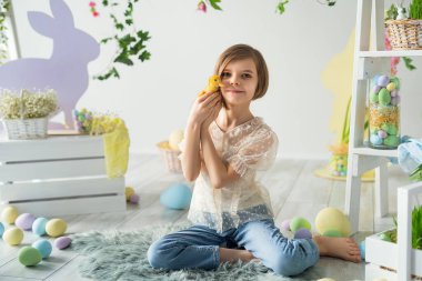 Gülümseyen kız yerde otururken ördek yavrusuyla iletişim kuruyor. Paskalya dekorasyonu. 