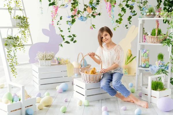 Little girl holds the basket with fluffy ducklings while sits on the wooden box. Easter decoration. — Stock Photo, Image