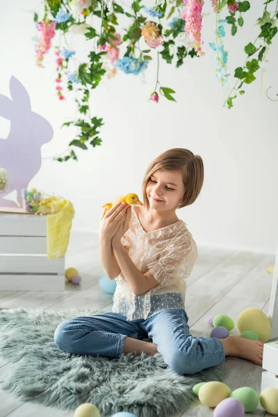 Happy child plays and communicates with duckling while sits on the floor. Easter decoration. — Stock Photo, Image