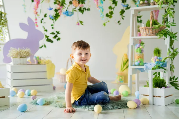 Petit garçon assis sur le sol en bois dans le studio de Pâques décoration avec des fleurs, lapins en bois, œufs — Photo