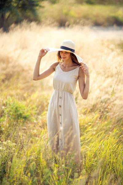 Jovem bela fêmea caminha em campo no verão, enquanto vestindo um chapéu de sol e vestido midi. Estilo de vida — Fotografia de Stock
