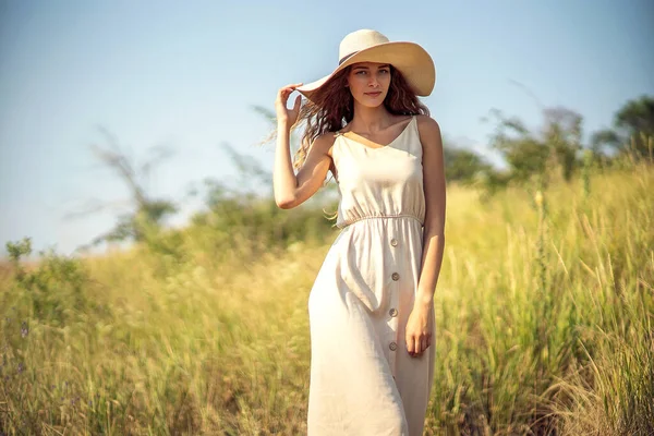 Jovem bela mulher caminha em campo no verão, enquanto vestindo um chapéu de sol e vestido midi. Estilo de vida — Fotografia de Stock