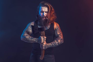 Yakışıklı adam yaşlı baltayı tutuyor. Sakallı oduncu. Uzun saçlı, dövmeli, ciddi bir erkek..