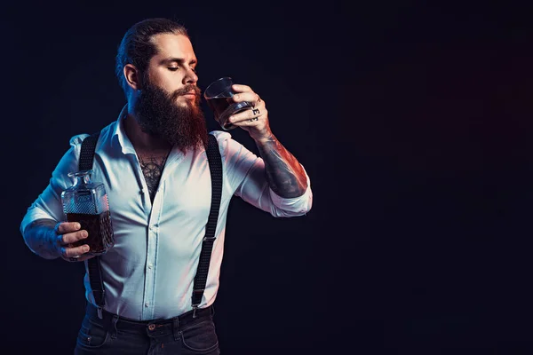 Bearded man holds bottle of whiskey in his hand and drinks dressed in white shirt. Studio shot — Zdjęcie stockowe