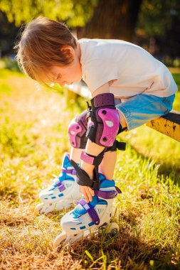 Çocuk kız bankta otururken paten giyer. Aktif sağlıklı yaşam tarzı. Güvenli sürüş
