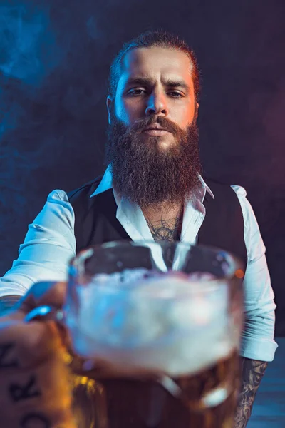 Serious bearded man holds out tasty draft beer to the camera. Drinking, October fest concept. — Zdjęcie stockowe