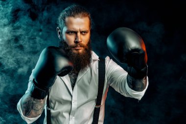 Serious bearded man in white shirt wears boxing gloves and ready to fight in smoke. Man self defense