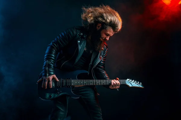 Expressive man rock guitar player with long hair and beard plays on the smoke background. Studio shot — Stock Photo, Image