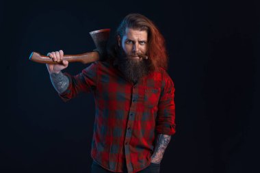 man with cigar holds old axe. Bearded lumberjack. Serious man in checkered shirt with long hair