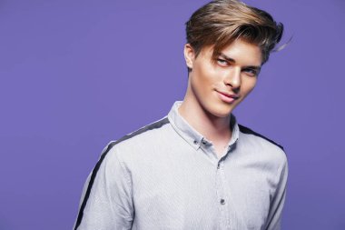 Mor arka plandaki kameraya bakarken gömlek giyen yakışıklı bir genç. Şık saç stili. 