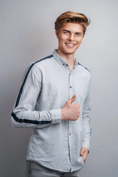 Portrait of a handsome smiling man standing shows thumb-up, isolated on a gray background. — Stock Photo, Image