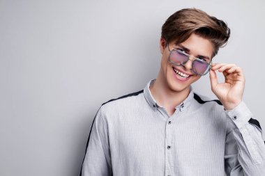 Erkek aksesuarları, optikler. Gömlekli ve modern güneş gözlüklü yakışıklı bir genç. Stüdyo resmi