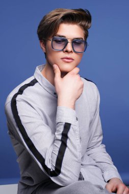 Erkek aksesuarları, optikler. Şık güneş gözlüklü, tişörtlü hippi adam. Stüdyo resmi.