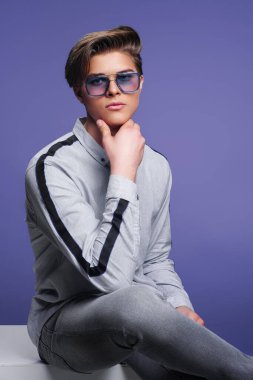 Erkek aksesuarları, optikler. Modern güneş gözlükleriyle oturan yakışıklı genç adam. Stüdyo resmi