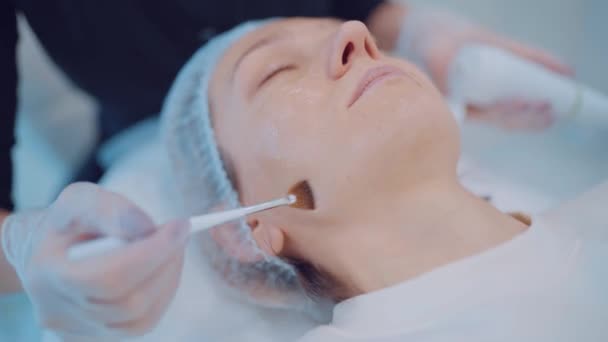 Close-up van cosmetoloog handen zet vochtinbrengende boter op meisje gezicht door borstel. Cosmetische procedure — Stockvideo