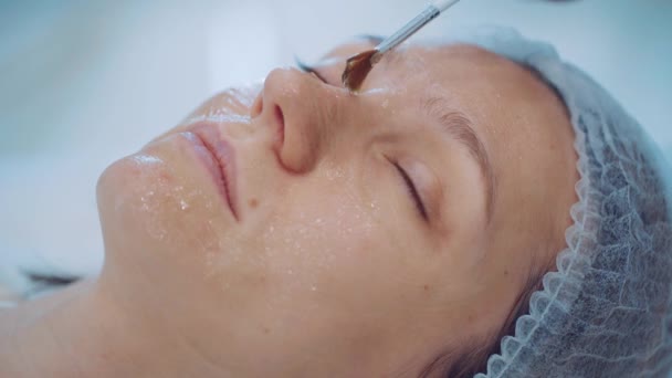 Close-up van cosmetoloog handen zet vochtinbrengende boter op meisje gezicht door borstel. Huidverzorging. — Stockvideo