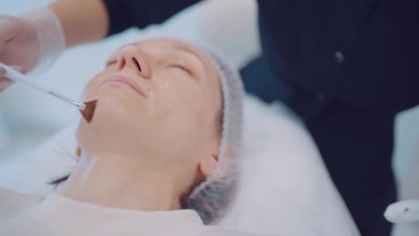 Close-up van cosmetoloog handen zet vochtinbrengende boter op meisje gezicht door borstel. Huidverzorgingsconcept — Stockvideo