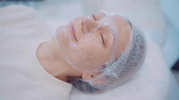 Mooi meisje met cosmetisch masker op haar gezicht ontspannen in beauty clinic. Huidverzorging — Stockvideo