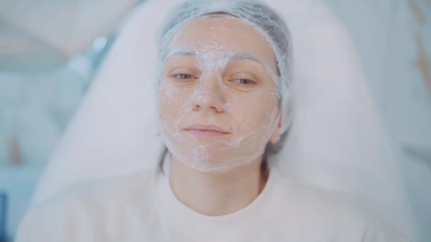 O femeie tânără frumoasă naturală, cu mască cosmetică pe față, se relaxează în clinica de frumusețe. Îngrijirea pielii — Videoclip de stoc