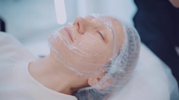 The beautician makes the girl face mask. Beautiful girl with cosmetic mask on her face. Skin care — Stock Video