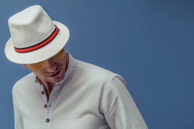 Güneş gözlüğü takan, renkli arka planda zarif beyaz şapkalı genç adamın stüdyo portresi.