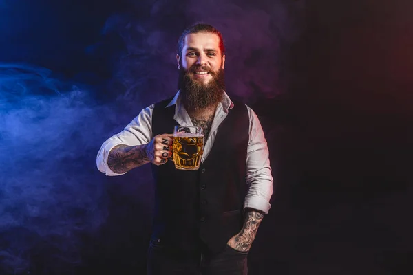 Uśmiechnięty brodaty mężczyzna trzyma w ręku smaczne piwo z beczki. Picie, październikowy festiwal koncepcyjny. — Zdjęcie stockowe