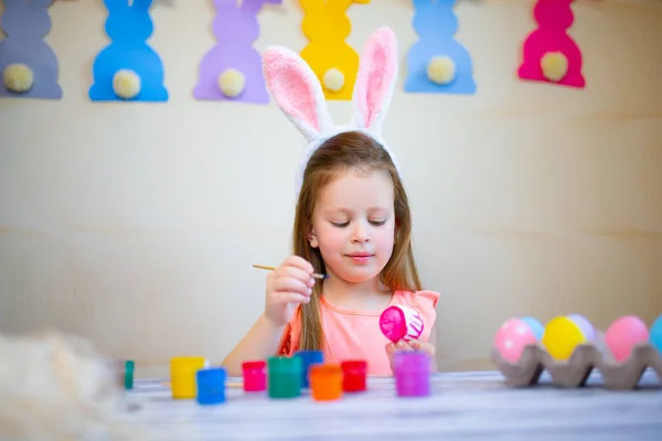 Dziewczynka w wielkanocnych uszach króliczka malowanie pisanek w domu przygotowuje się do Wielkanocy. Wesołych Świąt — Zdjęcie stockowe