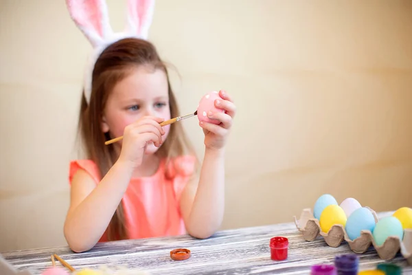 Симпатична дівчина у великодніх вухах малює великодні яйця вдома готується до Великодня. Щасливого Великодня — стокове фото