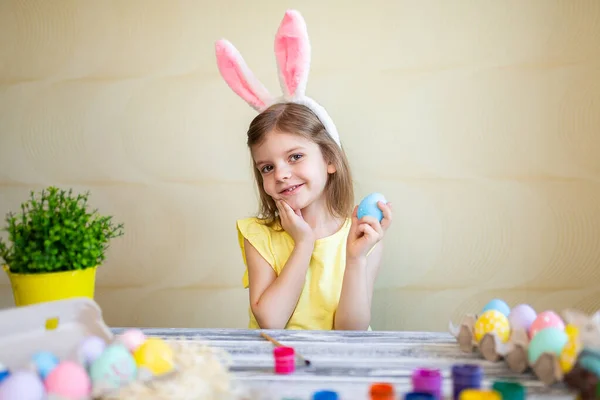 Dziewczynka w króliczych uszach trzyma wielkanocne jajko w dłoni patrząc w kamerę. przygotowanie do Wielkanocy — Zdjęcie stockowe