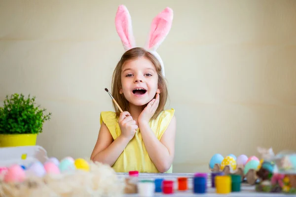 Забавна маленька дівчинка у вухах кроликів готується до Великодня розмальованих великодніх яєць. Зі святом Великодня концепція — стокове фото