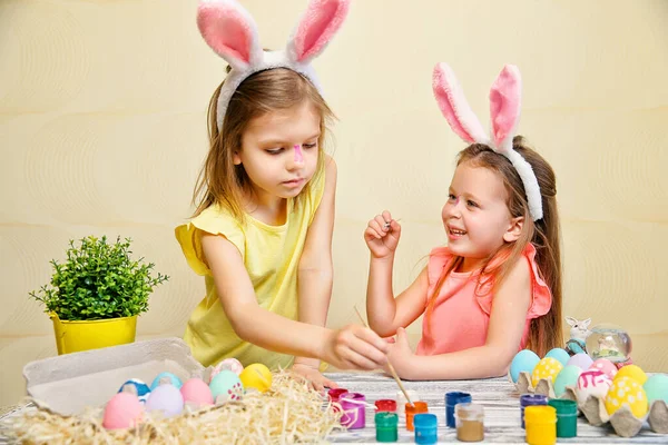 Dzieci w uszach króliczków malują wielkanocne jajka i obmacują się nawzajem. Przygotowuję się do Wielkanocy. Koncepcja wielkanocna — Zdjęcie stockowe