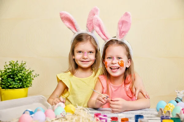 Dwie słodkie dziewczyny w farbie zabawy i udekorować pisanki podczas noszenia królicze uszy. Przygotowania do Wielkanocy — Zdjęcie stockowe