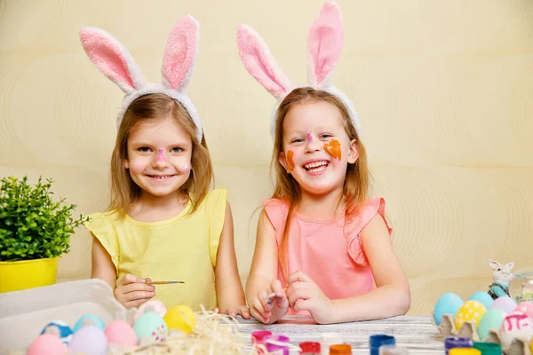 Dwie dziewczynki w zabawnej farbie i ozdobić pisanki podczas noszenia królicze uszy. Przygotowania do Wielkanocy — Zdjęcie stockowe