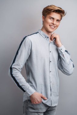 Gri arka planda duran ve poz veren şık, güler yüzlü, beyaz, yakışıklı genç bir adamın portresi. 