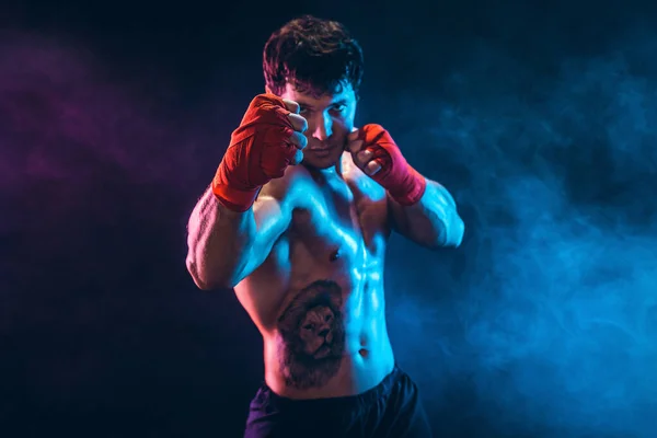 Retrato de kickbox musculoso o luchador tailandés muay que golpea sobre el fondo de humo. Concepto deportivo. — Foto de Stock