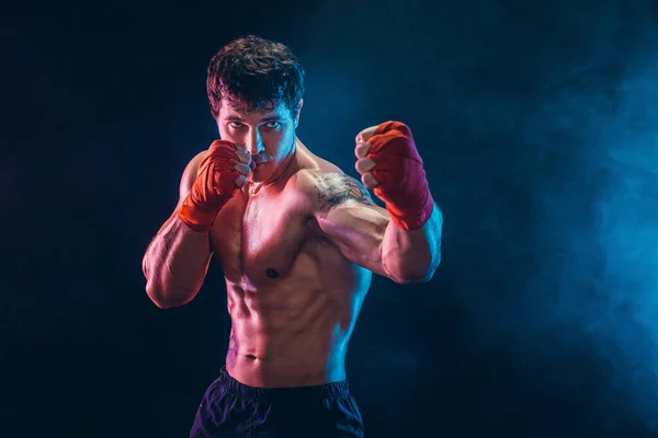 Retrato de kickbox musculoso o luchador tailandés muay que golpea en la oscuridad. Concepto deportivo. — Foto de Stock