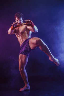 Diz vuruşu yapan kickboksör dövüşçüsü tam boy duman arka planda izole edildi. karışık ortam 