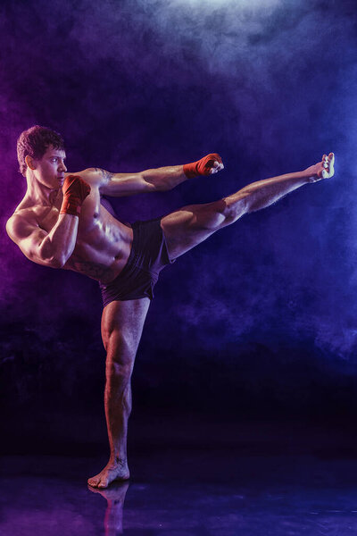 Полноразмерный кикбоксер, наносящий удар ногой по голове на фоне дыма. смешанные СМИ 