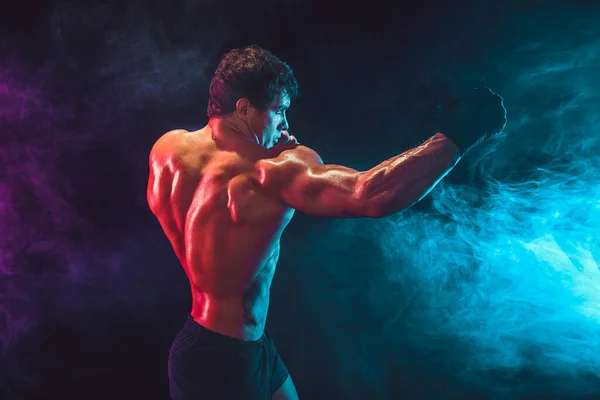 Boční pohled na sportovce bez trička boxer, který přináší hit úder na kouř pozadí. Sportovní koncept — Stock fotografie