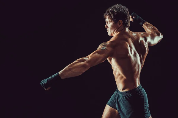 Vista lateral de agresivo boxeador muscular que golpea aislado sobre fondo oscuro. Concepto deportivo — Foto de Stock