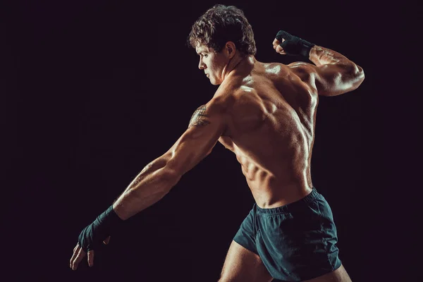 Vista lateral de boxeador musculoso sin camisa que golpea aislado sobre fondo oscuro. Concepto deportivo — Foto de Stock