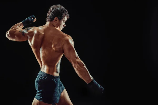 Vista lateral de atleta boxeador sin camisa que golpea aislado sobre fondo oscuro. Concepto deportivo — Foto de Stock