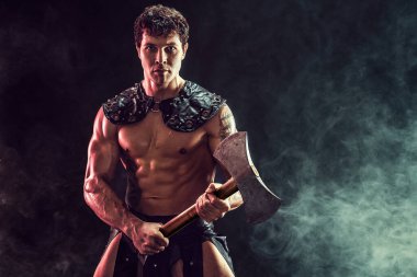 Elinde balta tutan ve arka planda poz verirken kameraya bakan seksi genç savaşçının portresi.. 