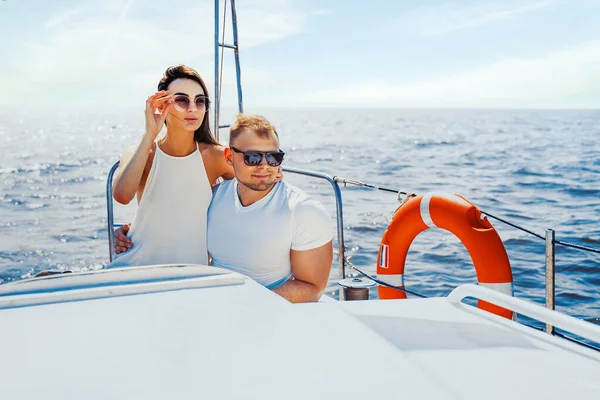 Mavi denize bakarken beyaz elbiseli mutlu genç çift yatta birlikte oturuyorlar. Seyahat