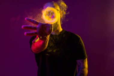 Genç adam eliyle bir duman halkasına uzanıyor. Renk filtreleri. Vaping konsepti 