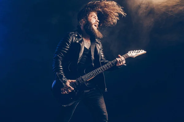 Emotional man rock guitar player with long hair and beard plays on the smoke background. Studio shot — Stock Photo, Image